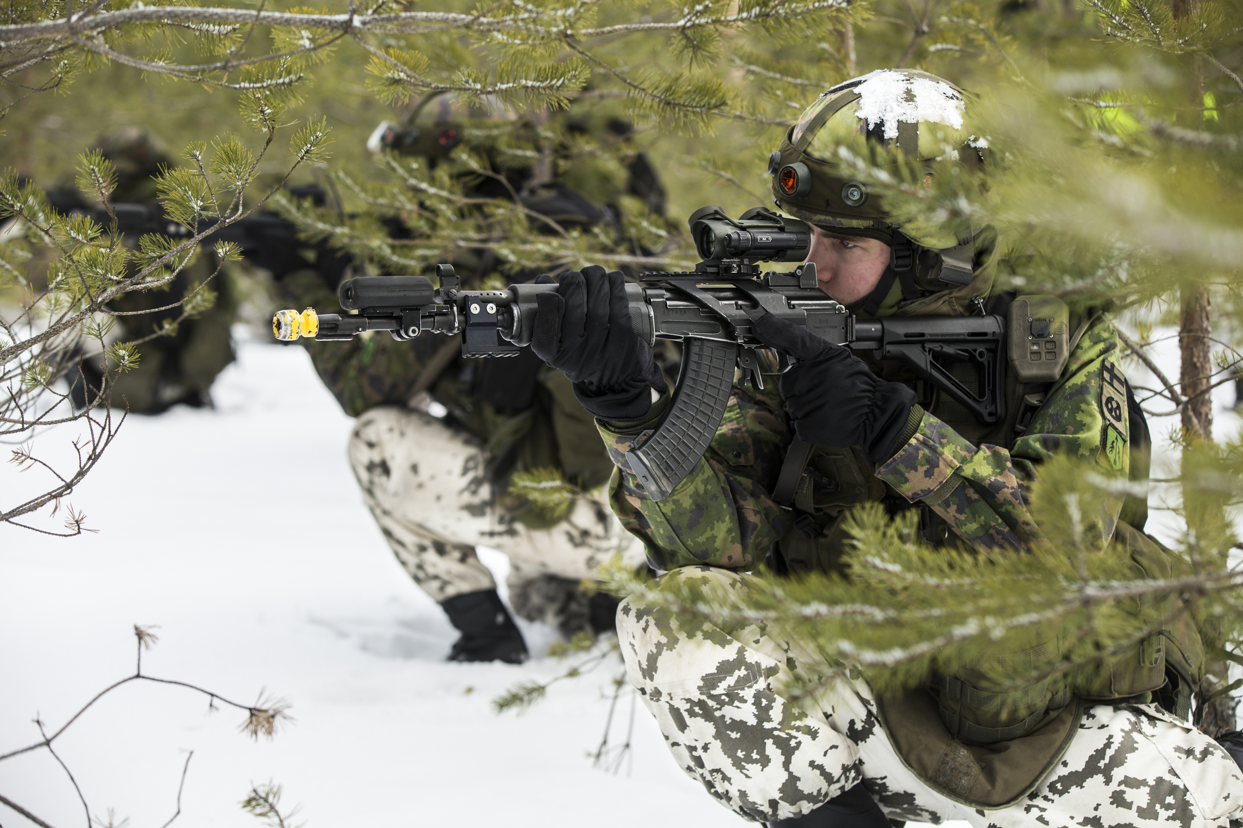 Sotilaat tähtäävät rynnäkkökivääreillä polviasennosta lumisessa metsässä