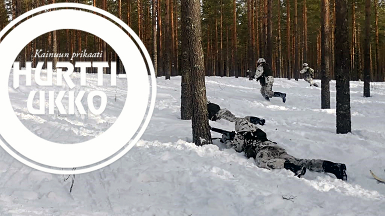 Lumipukuisia varusmiehiä taisteluharjoituksessa lumisessa metsämaastossa.