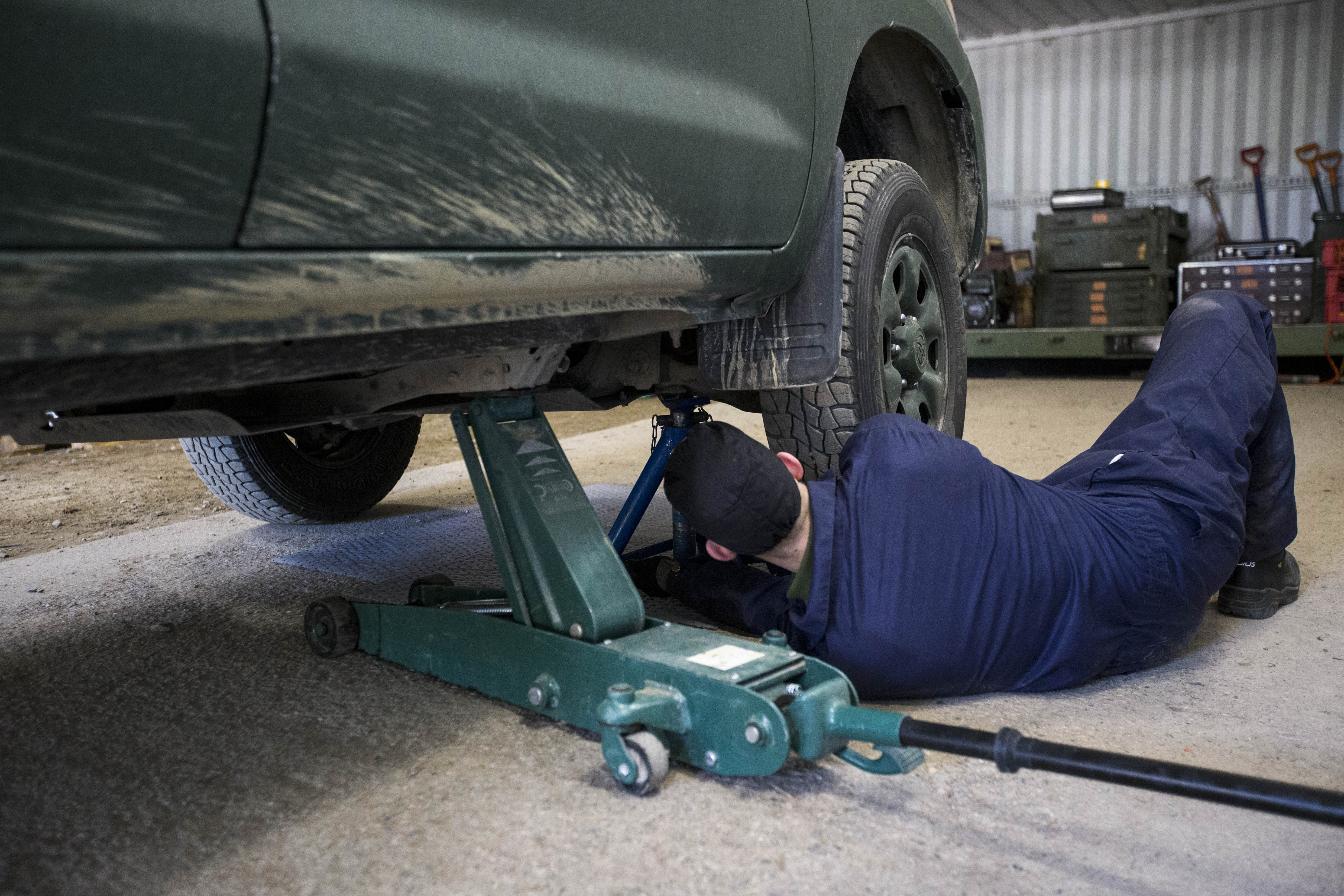 Mies sinisissä haalareissa korjaa autoa joka on nostettu tunkilla