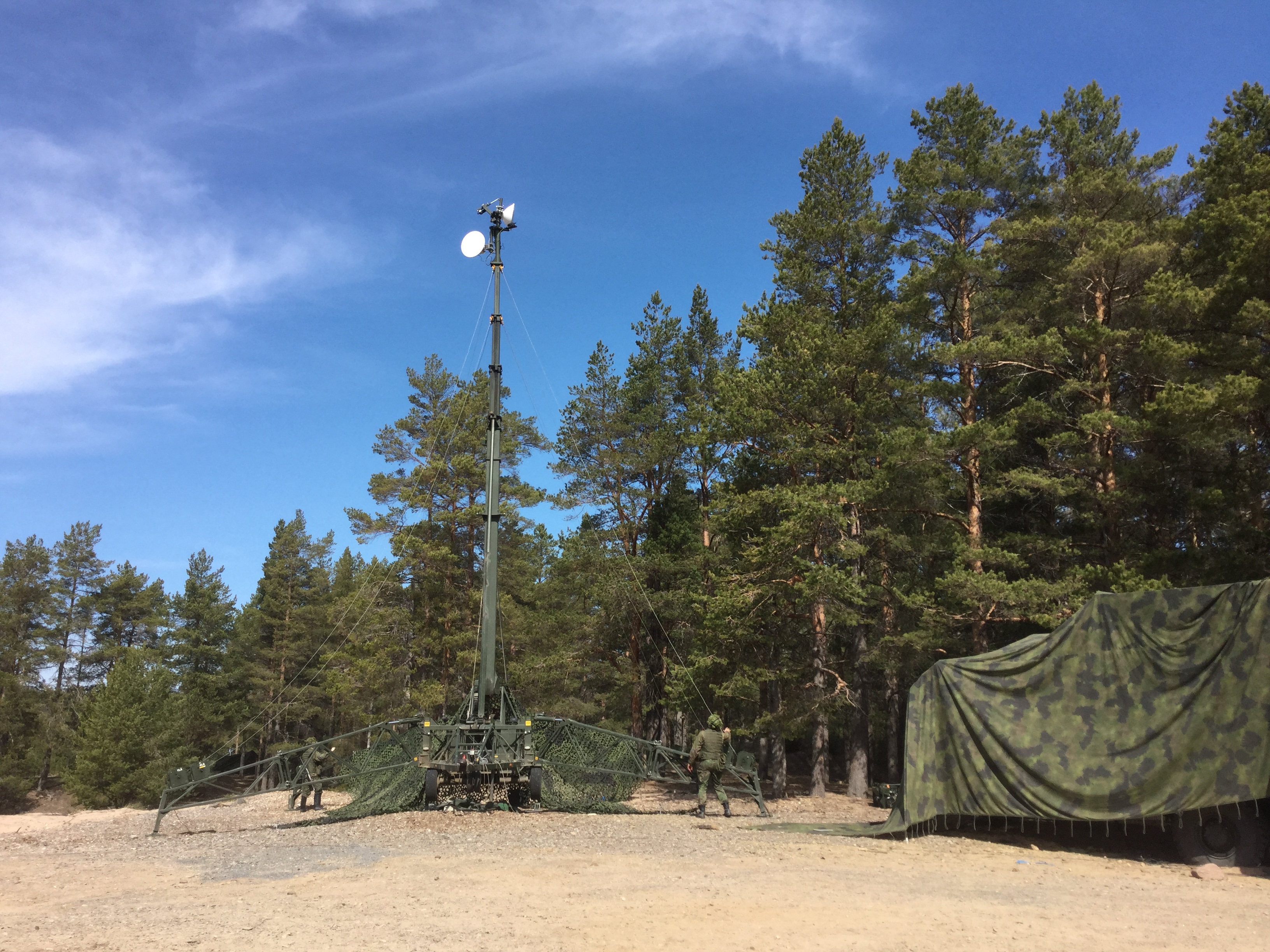 Sotilaat pystyttävät metsän reunalle mastoa jonka yläpäässä on antennilautasia