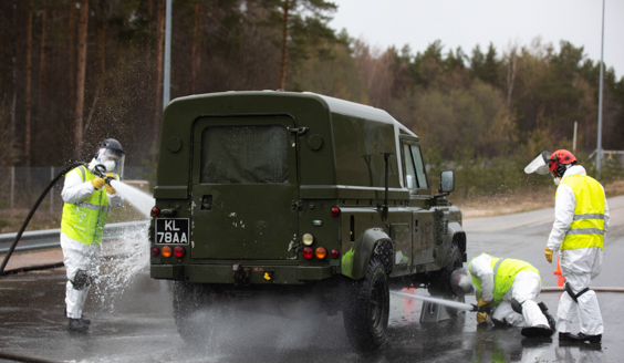 Suojavarusteisiin pukeutuneet henkilöt pesevät maastoautoa