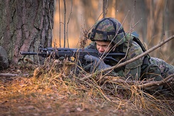 En värnpliktig från en idrottsskola siktar med ett automatgevär ute på fältet.