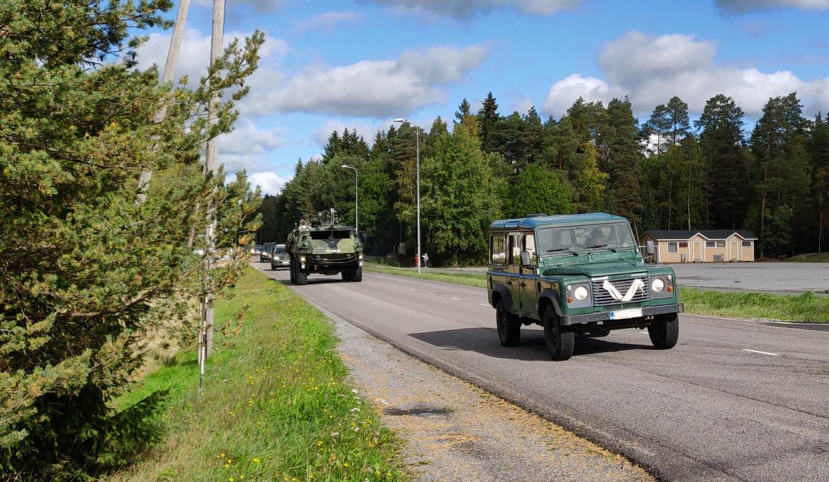 Kuvituskuva, jossa on Puolustusvoimien ajoneuvoja liikkeellä taajamassa.