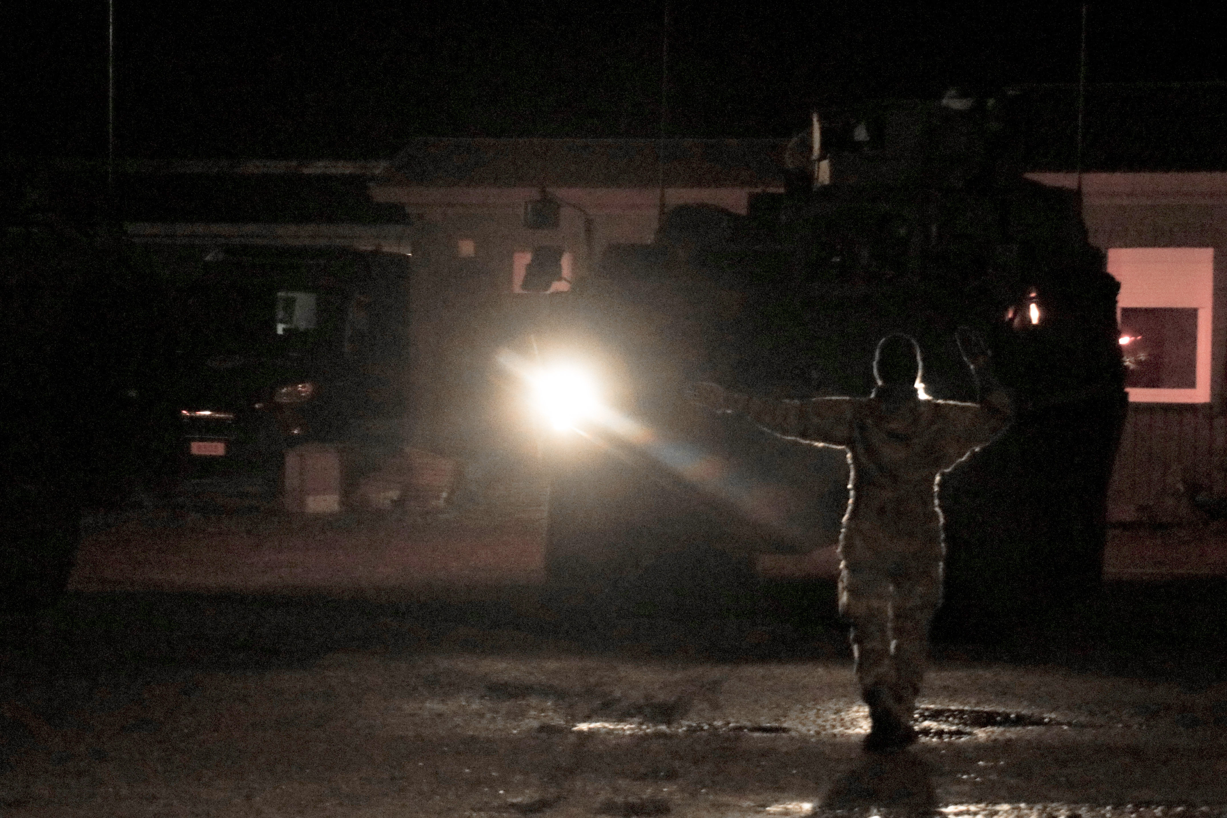 En dansk soldat vägleder med handtecken ett fordon i kvällsmörkret. 