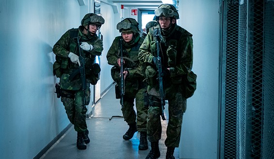 Kuvassa kolme sotilasta aseineen etenee sisätiloissa käytävää pitkin.