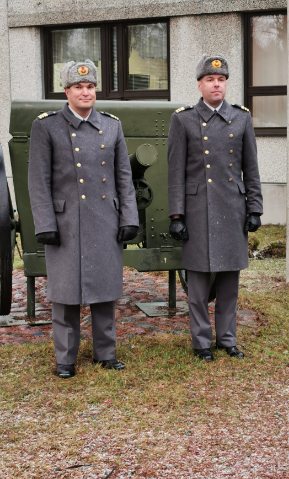 Kaksi sotilashenkilöä seisoo ja poseeraa tykin edessä.