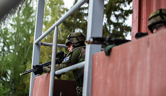 Varusmies tähtää aseella rakennuksesta