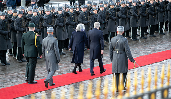 Tasallan presidentti kulkee punaisella matolla vieraan kanssa, taustalla maavoimien kunniakomppania rivimuodostelmassa.