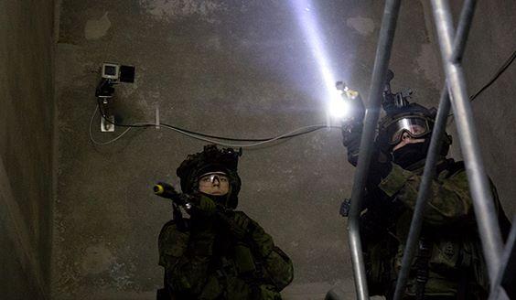 Two soldiers in a dark stairway. One has a flashlight on his gun.