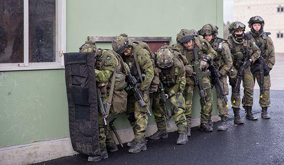 Soldiers next to a building wall. First one has a shield.