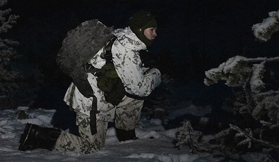 sotilas lumipuvussa pimeässä metsässä polviasennossa