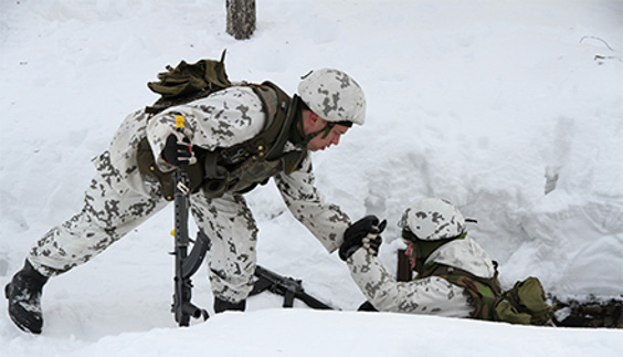 Sotilas auttaa toista sotilasta ylös lumesta