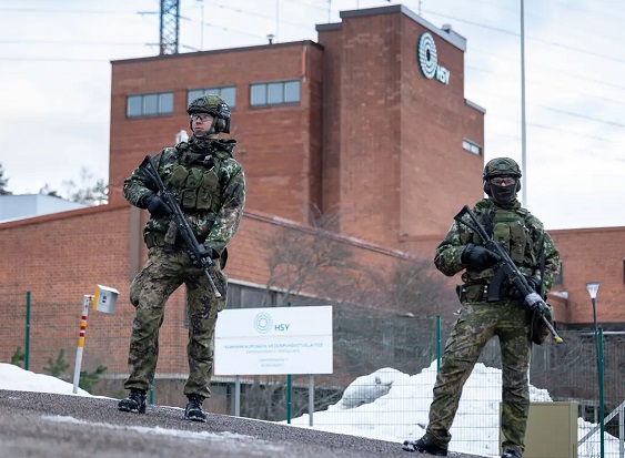 Kaksi asetta kantavaa sotilaspukuista henkilöä Helsingin seudun ympäristöpalvelujen rakennuksen edessä talviaikaan