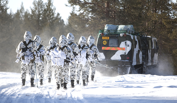 A vehicle pulling soldiers on skis with a rope