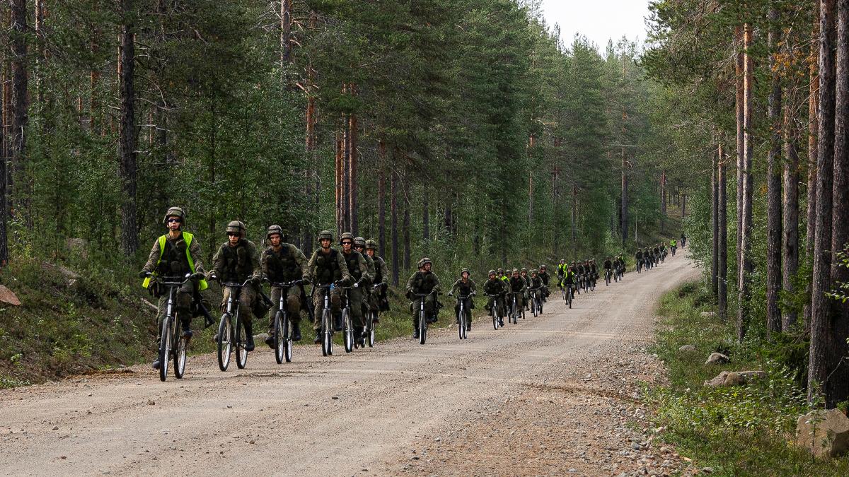 Varusmiehiä pyöräilemässä hiekkatiellä.