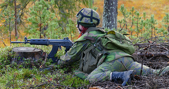 Naissotilas makaa maastossa rynnäkkökiväärin kanssa