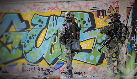 Kaksi sotilasta kaupunkiympäristössä, taustalla olevassa seinässä on graffiteja