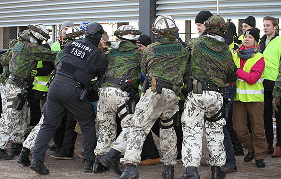 Sotilaspoliisit ja poliisi pitelevät kiinni ihmisistä, taustalla myös huomioliivisiä siviilejä.