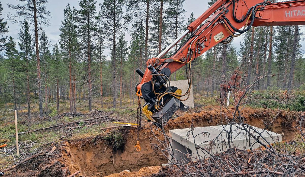 Kaivinkone kaivaa betoniselle suojalle kuoppaa maastossa.