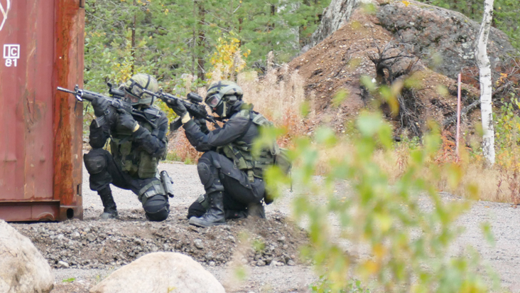 Kaksi sotilasta tähtää rynnäkkökivääreillä rakennuksen kulmalla.