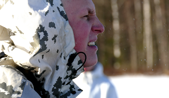 A soldier in a snow suit squints his eyes in the sun