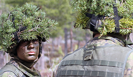 Soldiers in combat gear, helmets disguised with pine foliage