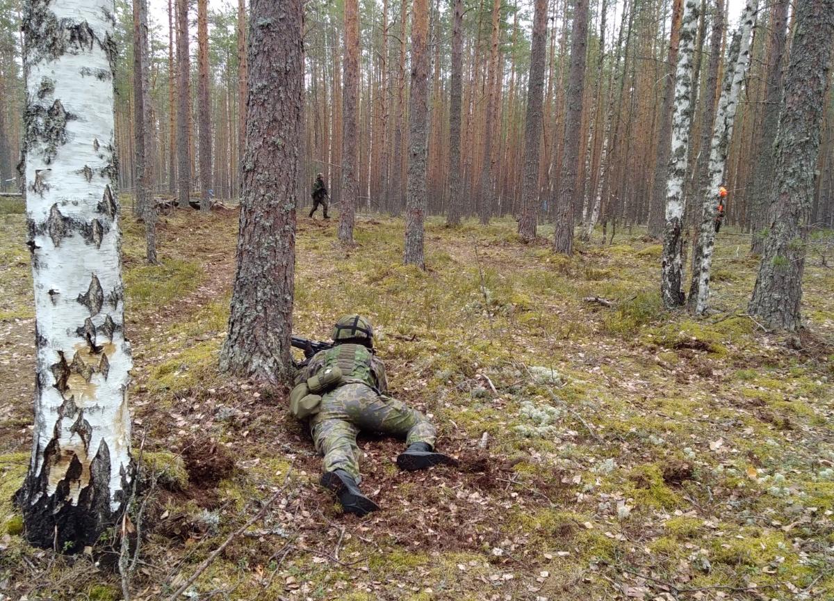 Taistelija tukee parinsa irtaantumista maastossa. Taistelija mahallaan maassa ja ampuu aseella.