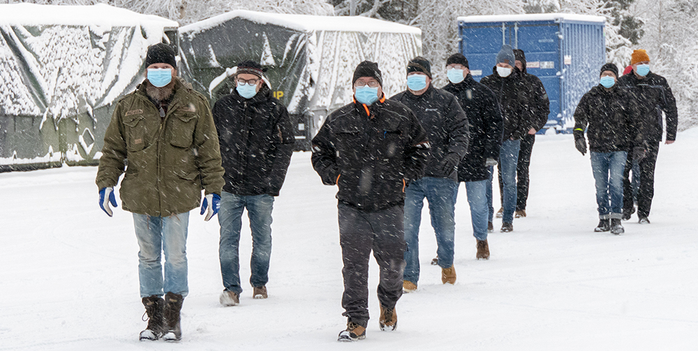 Kymmenen reserviläistä kävelee lumisateessa, he ovat menossa hakemaan kertausharjoitusvarustusta varastolta. Resreviläisillä on kasvomaskit.