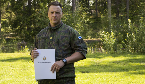 kuvassa vääpeli Jani Mäkinen seisoo ulkona opinnäytetyö kädessään