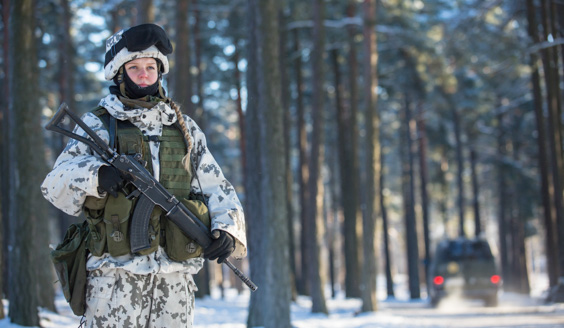 Naissotilas seisoo talvisessa metsässä taisteluvarustuksessa