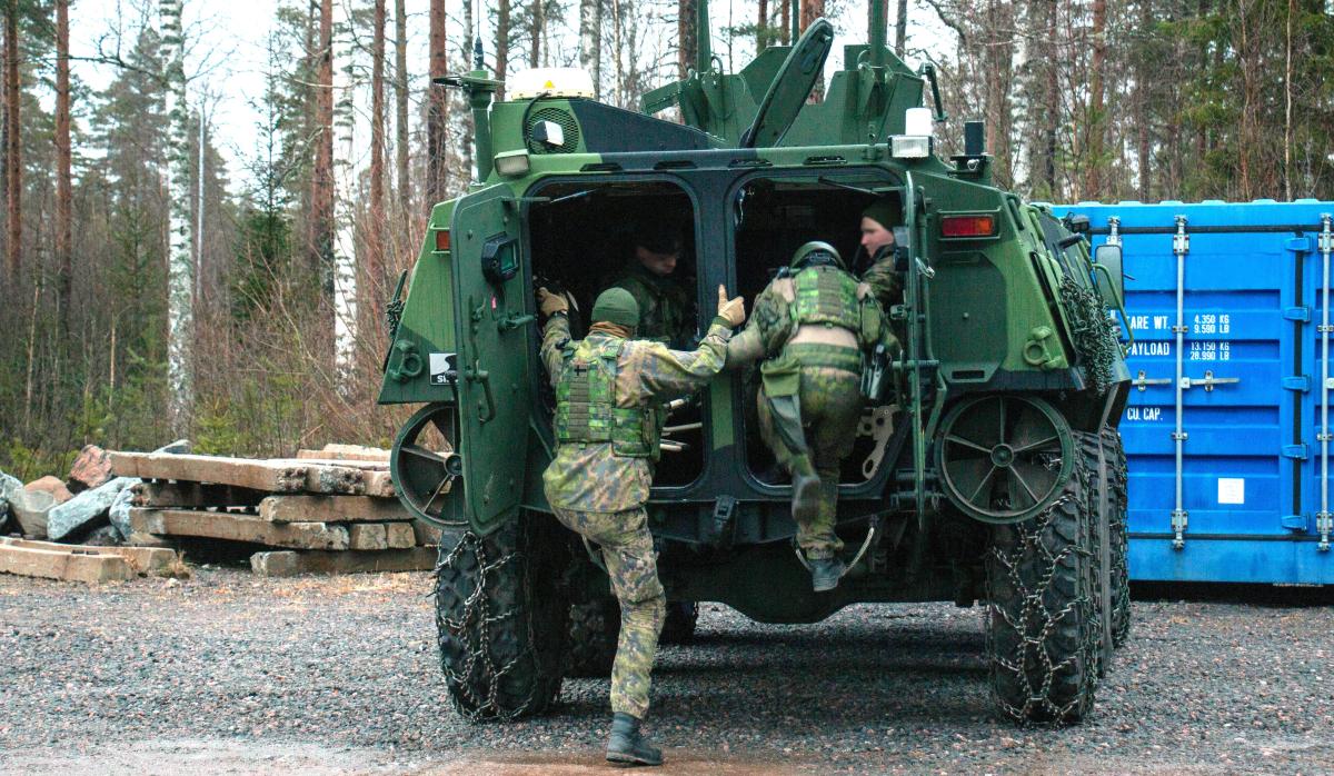 Two Finnish soldiers from the Armoured Reconnaissance Detachment are climbing into a armoured personnel carrier.
