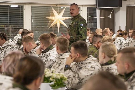 Maavoimien aliupseereiden perinnemestari on sotilasmestari Esa Ek, joka seisoo kuvassa maastopuvussa, lumipukuiset sotilaat istuvat ja kuuntelevat.