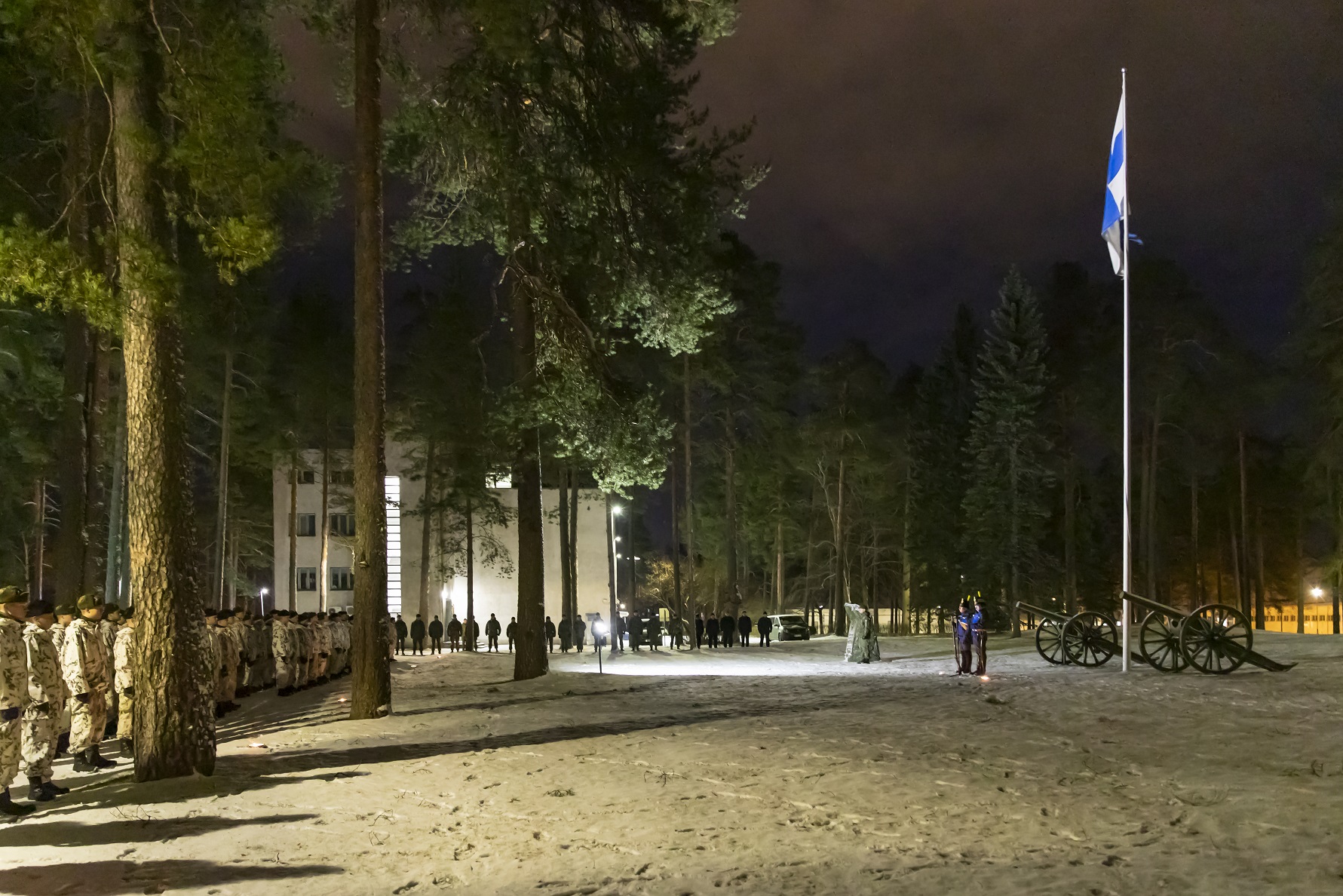 Rivissä sotilaita ja Suomen lippu lipputangossa aamuhämärässä.