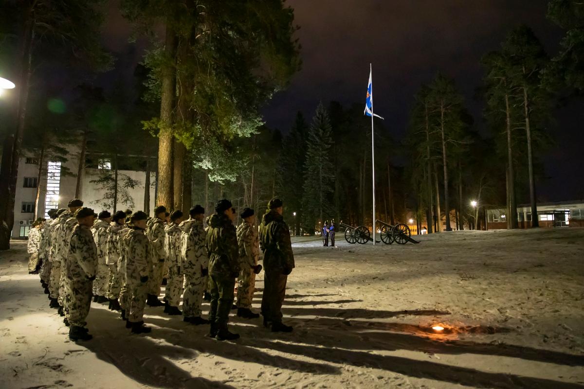 Rivissä lumipukuisia sotilaita ja edessä lipputangossa Suomen, puolustusvoimien lippu