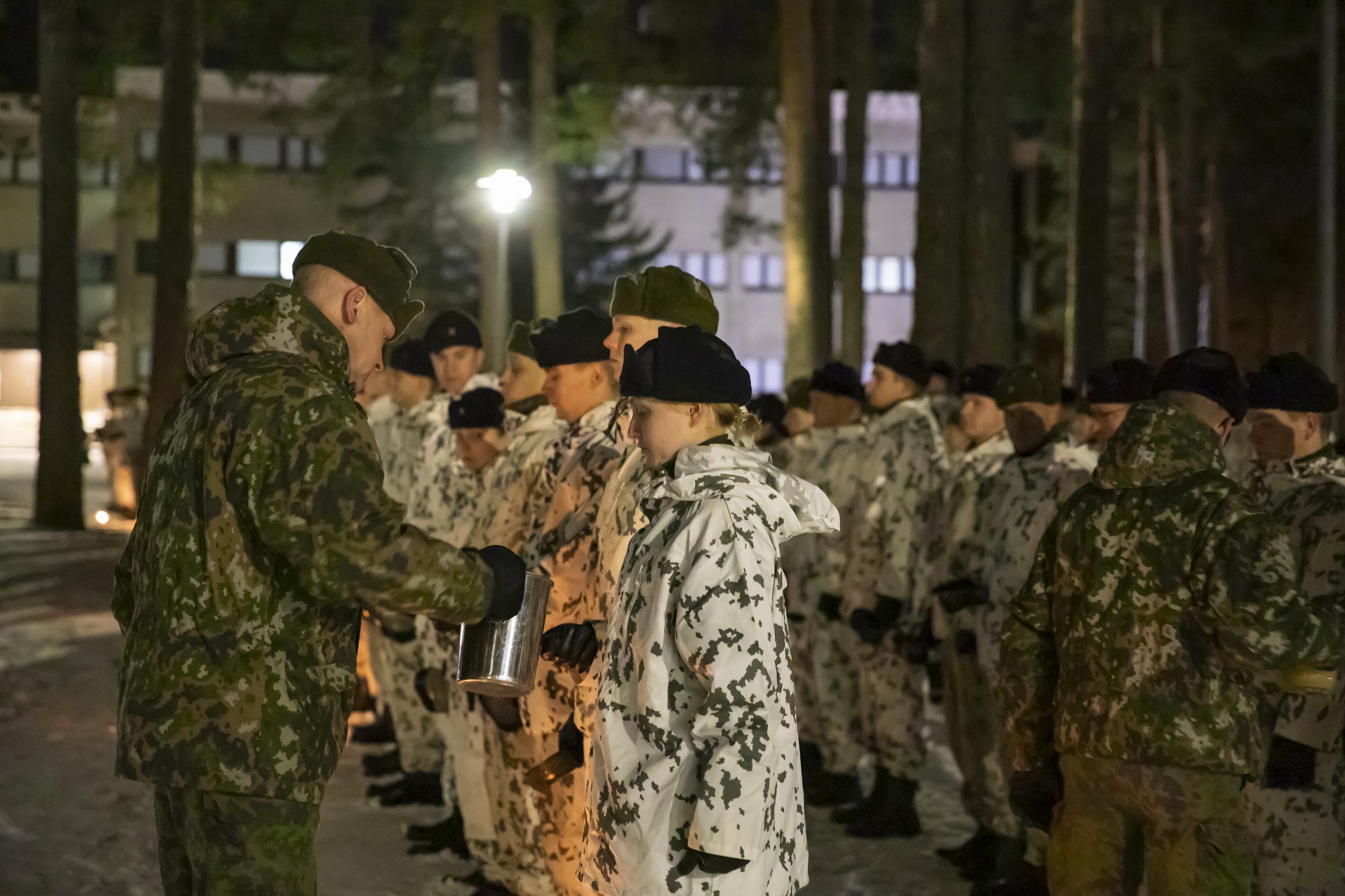 Sotilasmestari Esa Ek kaataa kannusta rivissä oleville sotilaille mukiin katkeraa kalkkia, aliupseerien perinnejuomaa.