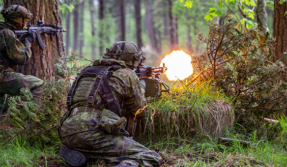 Kuvassa vuoden 2022 Sapeli-harjoituksen taisteluvaihe. Varusmiehet ampuvat aseella metsämaastossa puun suojasta.