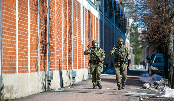 Kaksi sotilasta kävelemässä taisteluvarustuksessa kadulla aurinkoisessa kevättalvisessa säässä. Molemmat katsovat kameraan.