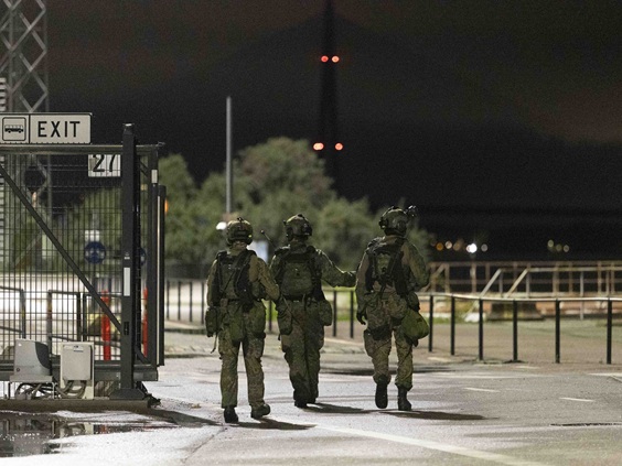 Militärpolis utför en säkerhetsuppgift i ett stadsområde: tre värnpliktiga rör sig utomhus i mörkret i stridsutrustning.