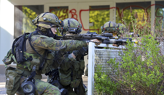 Kuvassa maastopukuisia sotilaita nojaamassa aitaan aseiden kanssa.