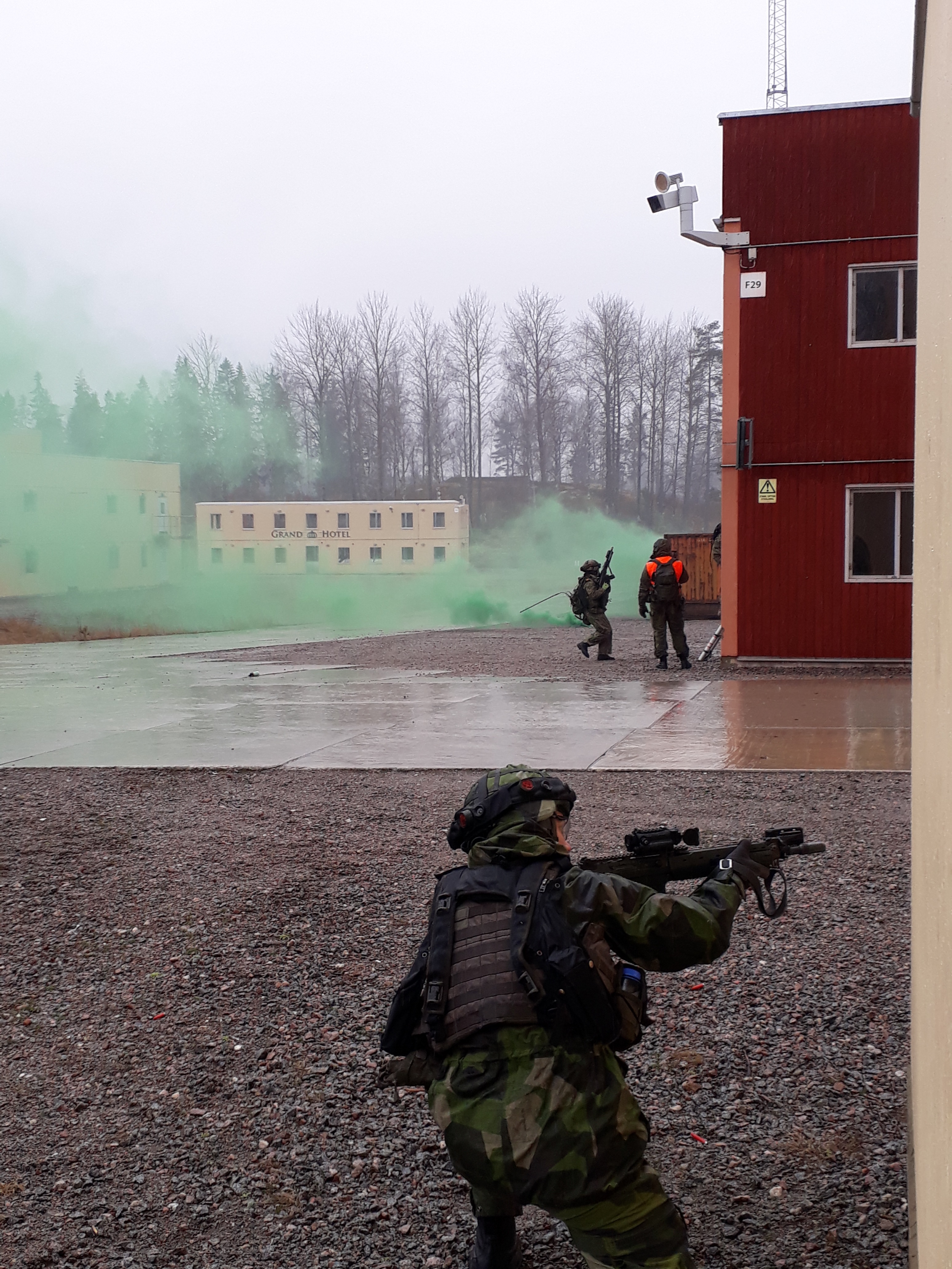Vihreää savua rakennetun alueen taisteluharjoitusalueella, kamera kuvaa, kun suomalaissotilaat harjoittelevat.