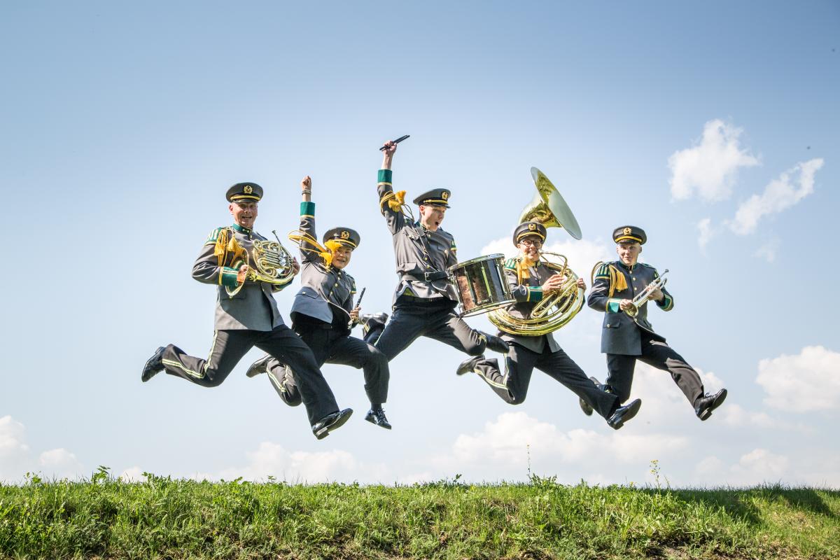 Rakuunasoittokunnan muusikot uniformuissaan hyppää ilmaan kauniissa aurinkoisessa säässä Lappeenrannan linnoituksessa.