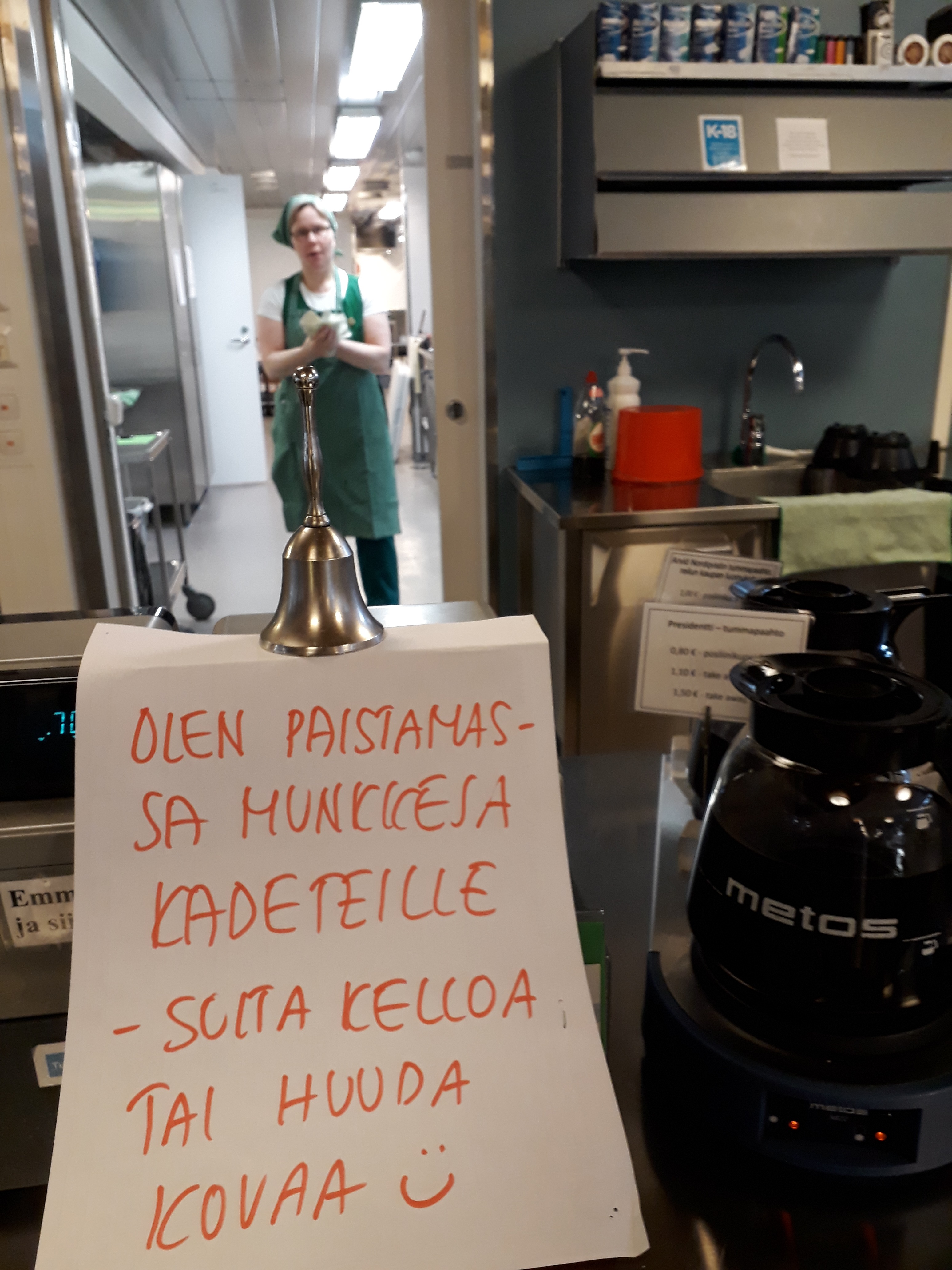 Sodes kassalla lappu, jossa Sikkuli sanoo: "Olen leipomassa kadeteille m unkkeja, soita kelloa tai huuda kovaa!" Hän on kassalle käsiään pyyhkien.