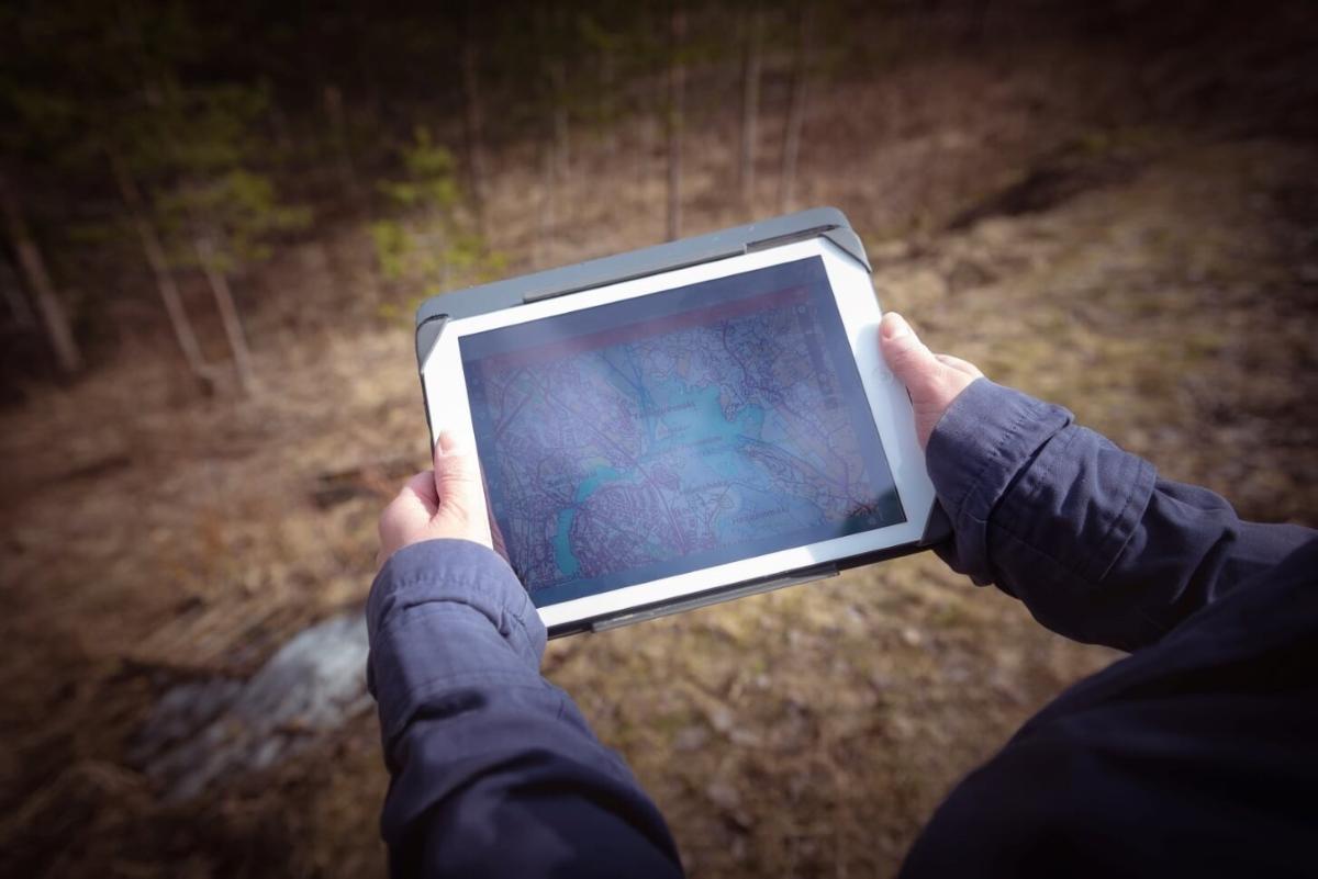 Kuvassa tunnistamaton henkilö pitää käsissään mobiililaitetta, jolla voi kerätä paikkatietoja maastossa.