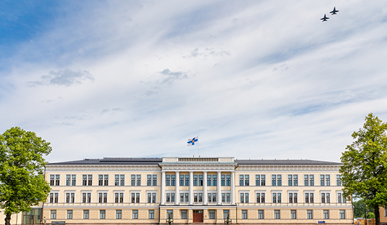 iso vaalea rakennus, jonka katolla Suomen lippu, taivaalla lentää kaksi hävittäjää