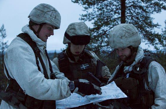 Kolme lumipukuista sotilasta lukee karttaa