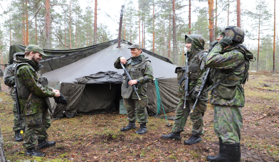 Viisi miestä keskustelee metsässä.