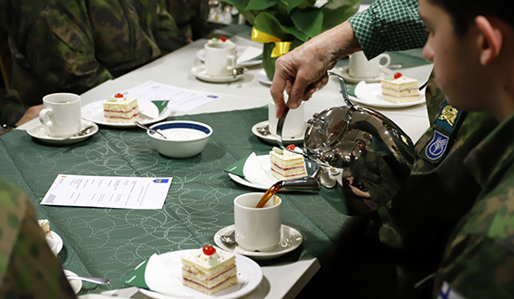 Sotilaskodin työntekijä kaatamassa varusmiehelle kahvia kuppiin. Pöydällä kakkupala.