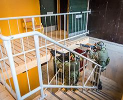Kaksi sotilaspoliisia osoittaa aseella portaikossa harjoitustalon yläkertaan.