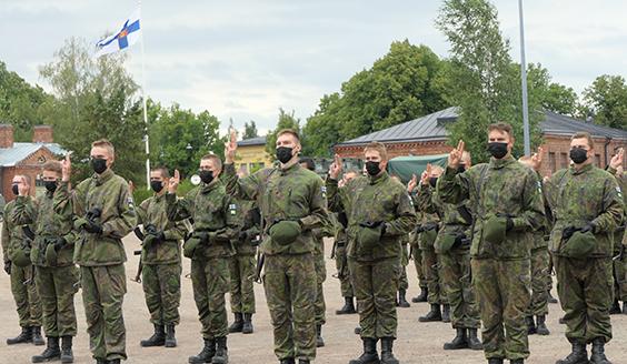 Varusmiehiä valanantoasennossa, taustalla rakennuksia ja Suomen lippu