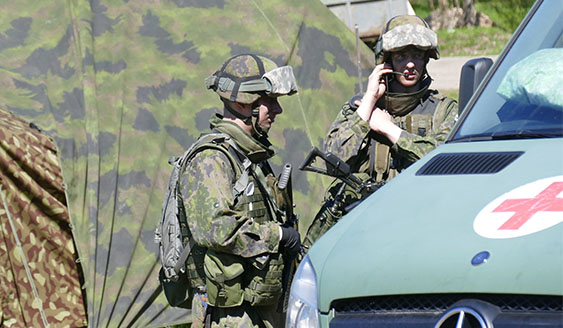 Kaksi sotilasta vihreän pakettiauton vieressä, jossa on punainen risti